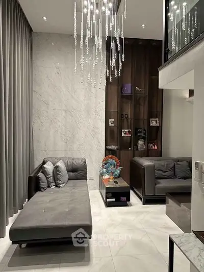Luxurious modern living room with high ceilings, elegant chandelier, and stylish gray furniture.