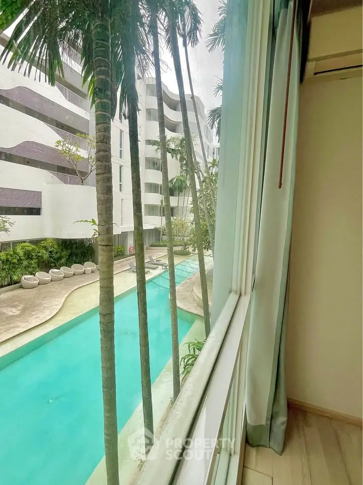 Luxurious poolside view from modern apartment window with palm trees and sleek architecture.