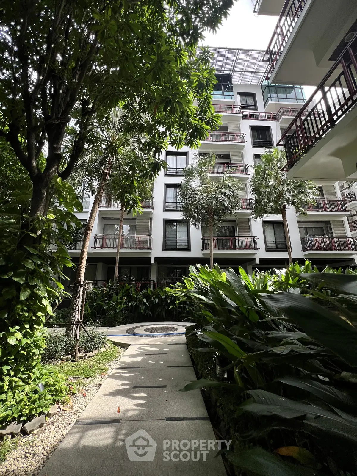 Lush garden pathway leading to a modern apartment building with balconies.