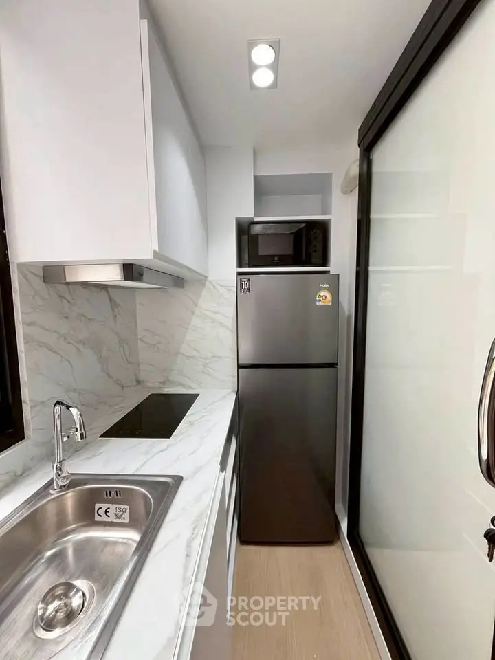 Modern compact kitchen with sleek appliances and marble countertops in a stylish apartment.