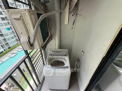 Compact balcony with washing machine and pool view in modern apartment complex.