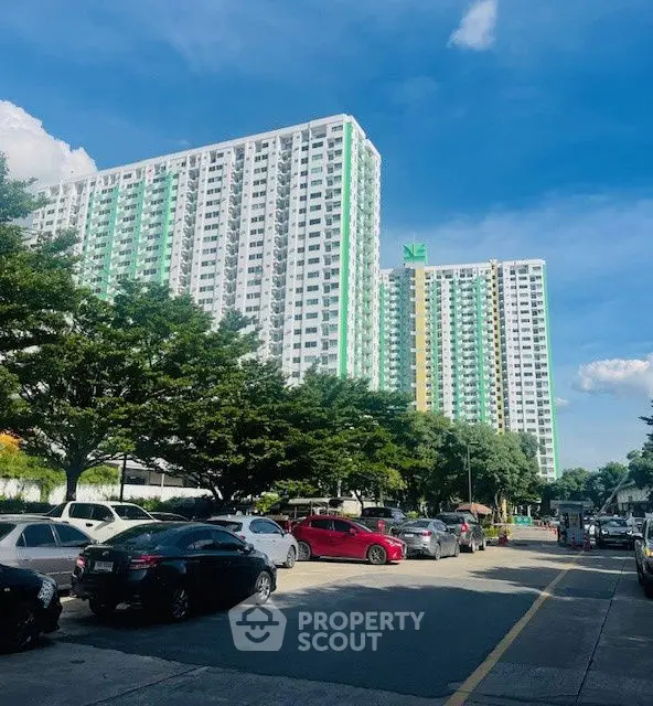 Modern high-rise residential building with ample parking and lush greenery.