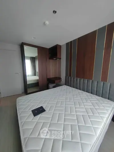 Modern bedroom with stylish wood paneling and mirrored wardrobe, featuring a comfortable mattress.