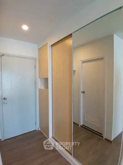 Modern apartment entrance with sleek mirrored closet and wooden flooring
