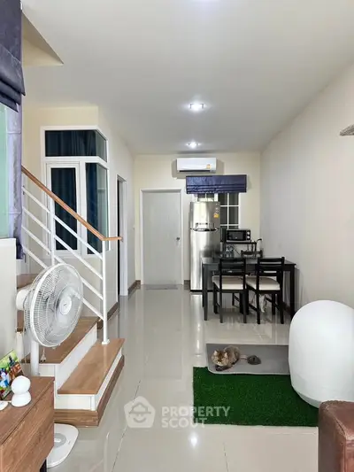 Modern living room with dining area and staircase, featuring sleek design and bright lighting.