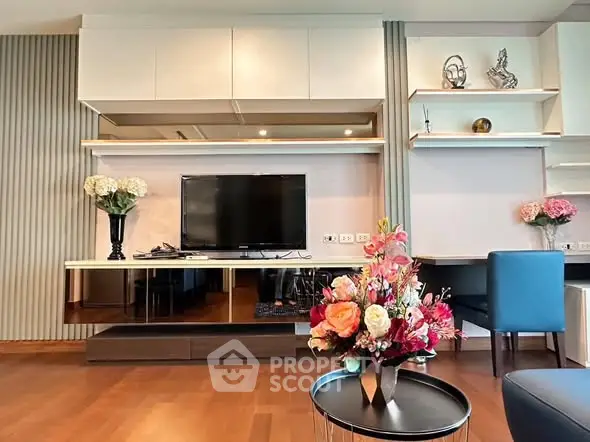 Modern living room with elegant decor, featuring a flat-screen TV, stylish shelving, and vibrant floral arrangements.