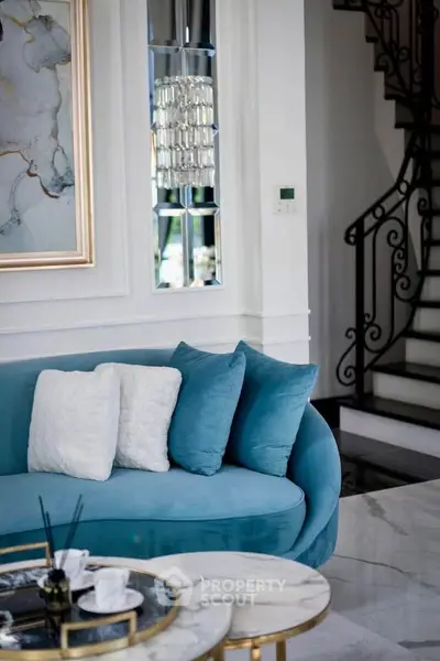 Elegant living room with plush blue sofa, chic marble table, and stylish staircase, perfect for modern luxury living.