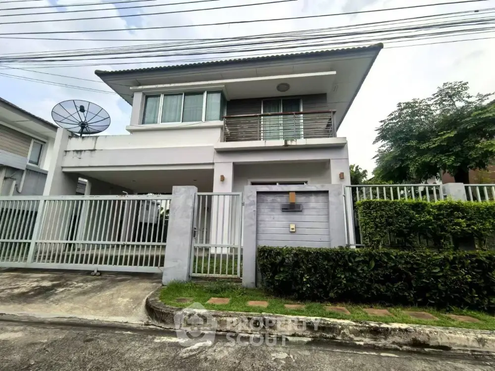 Modern two-story house with balcony and gated entrance in suburban neighborhood