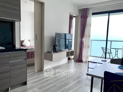 Modern open-plan living room with balcony and ocean view, featuring sleek furniture and natural light.
