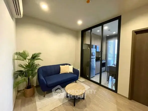 Modern living room with blue sofa and glass partition leading to kitchen