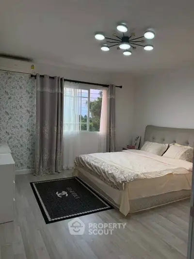 Cozy bedroom with elegant decor and ample natural light, featuring a stylish bed and modern lighting fixture.