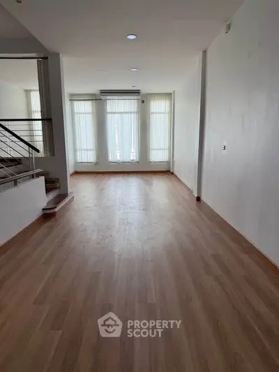 Spacious empty living room with wooden flooring and large windows, perfect for customization.
