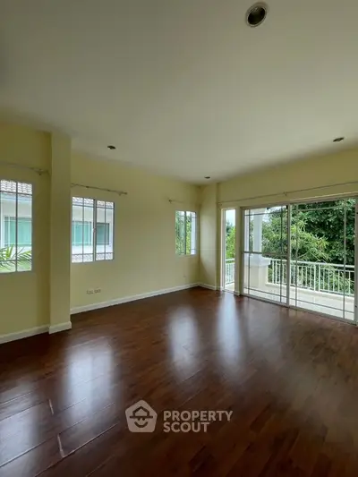 Spacious living room with hardwood floors and large windows overlooking lush greenery.