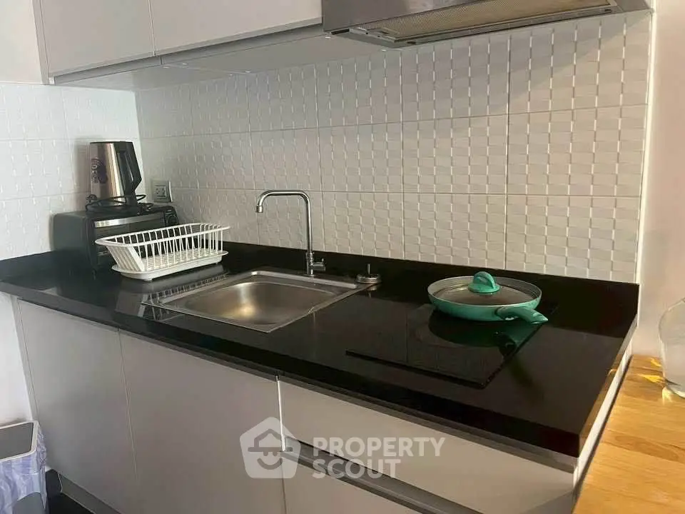 Modern kitchen with sleek black countertop and white cabinets, featuring a built-in sink and stylish backsplash.