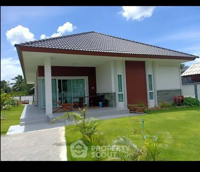 Charming modern house with lush green lawn and spacious porch under clear blue sky.