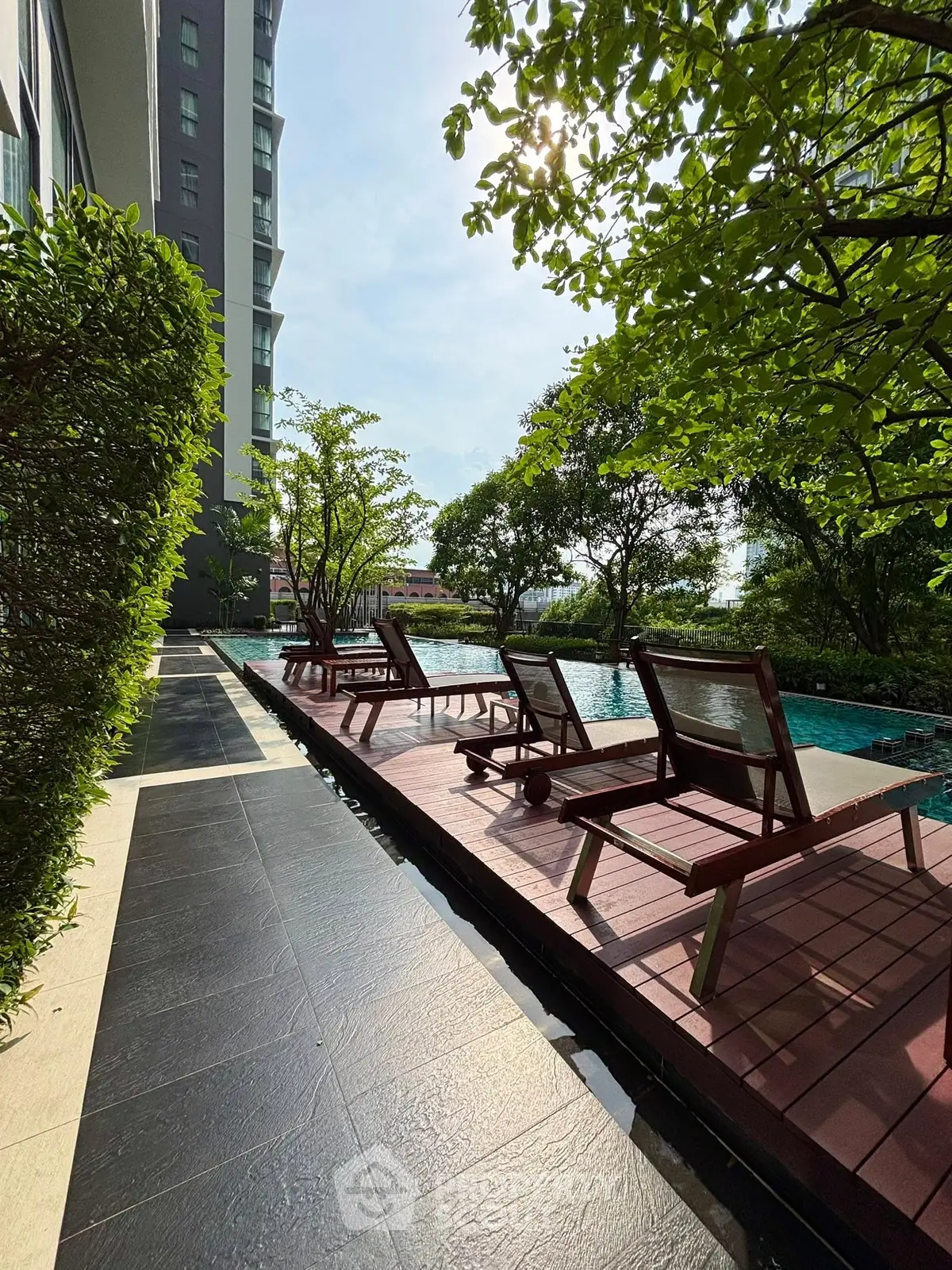 Luxurious poolside area with sun loungers and lush greenery in modern residential complex.