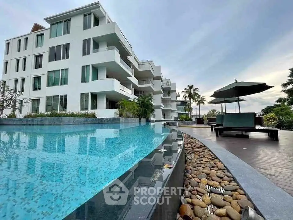 Luxurious modern apartment building with poolside view and lush greenery.