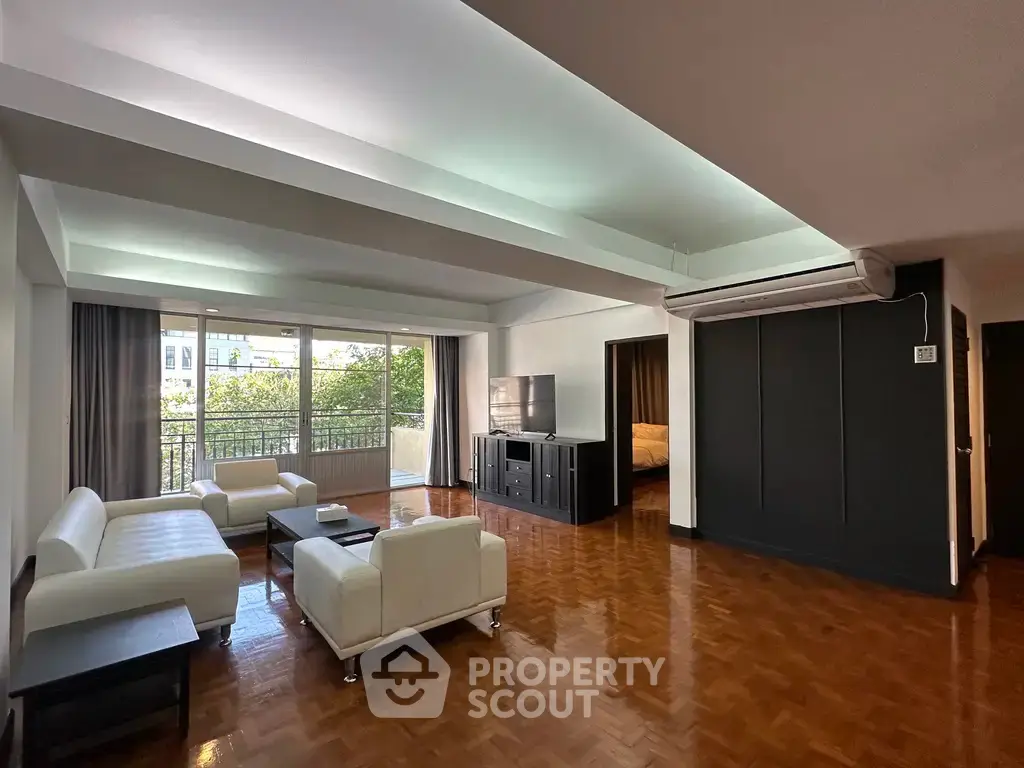 Spacious living room with modern furniture and large windows offering natural light and a view of greenery.