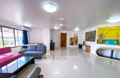 Spacious modern living room with stylish furniture and vibrant artwork, featuring large windows for natural light.