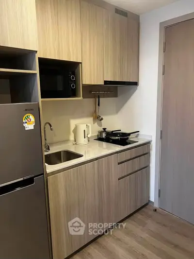 Modern compact kitchen with wooden cabinets and sleek appliances in a cozy apartment.