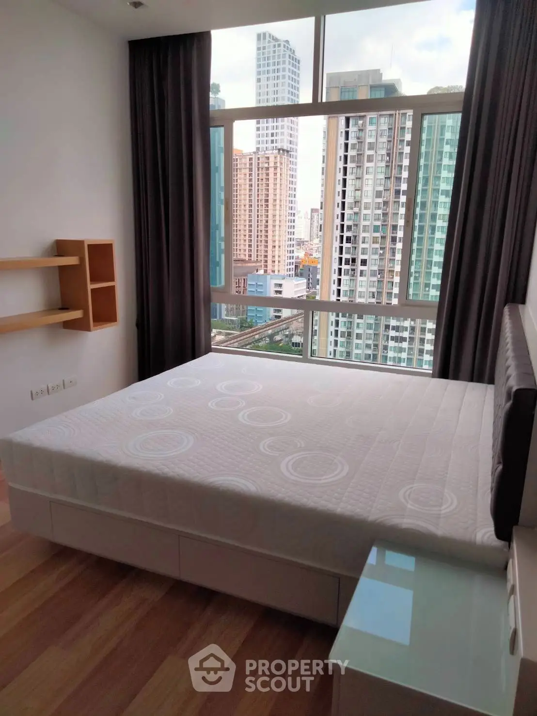 Modern bedroom with large window offering stunning cityscape view in high-rise apartment.