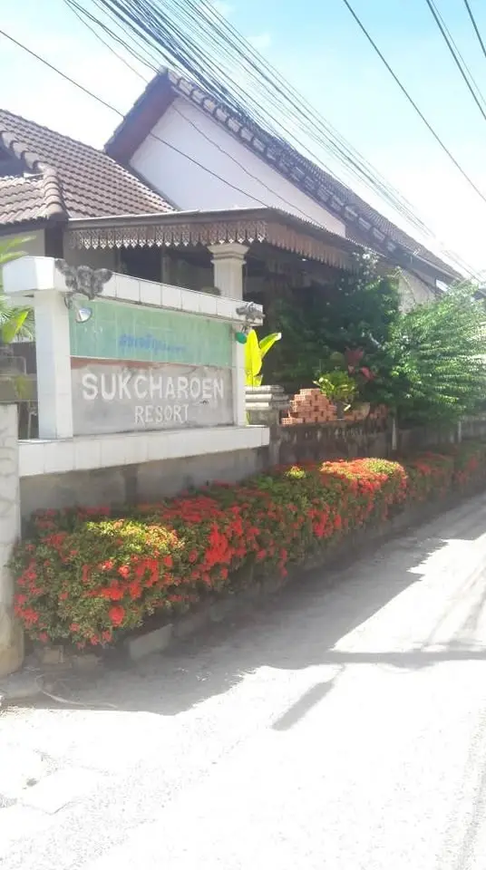 Charming Sukcharoen Resort entrance with lush greenery and vibrant flowers.