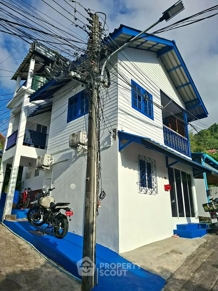 Charming blue and white house with balcony and motorcycle parked outside.