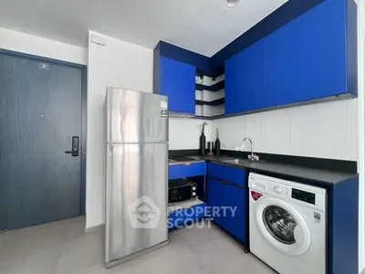 Modern kitchen with blue cabinets, stainless steel fridge, and washing machine.