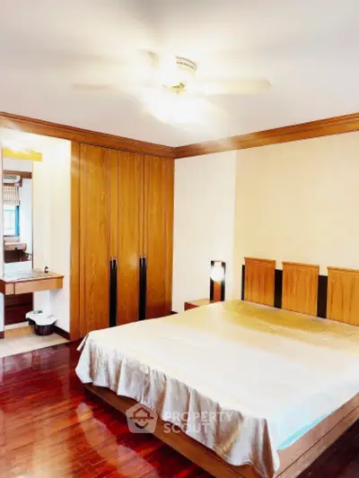 Spacious bedroom with wooden flooring and built-in wardrobe, featuring a ceiling fan and cozy ambiance.