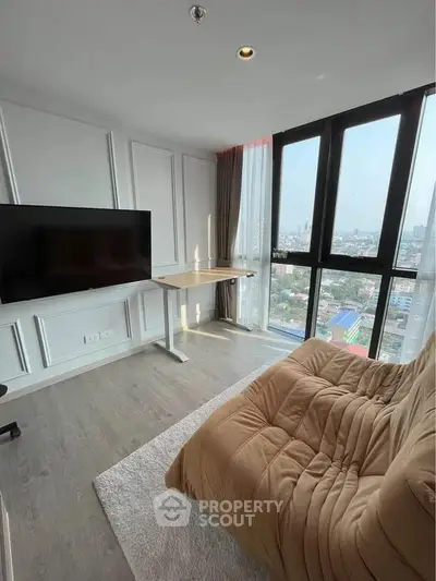 Modern living room with large windows and city view, featuring a cozy sofa and sleek TV setup.