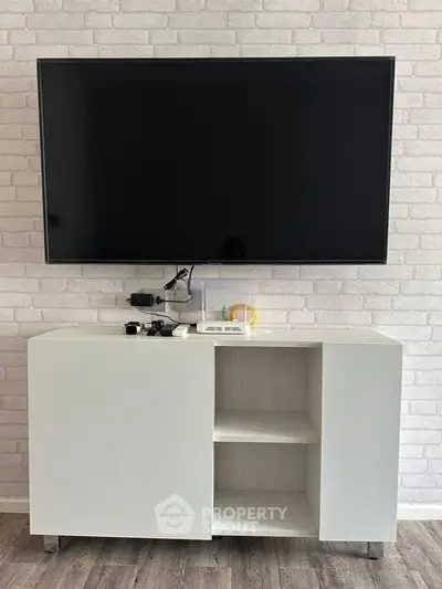 Modern living room with sleek TV setup and stylish white cabinet against brick wall.