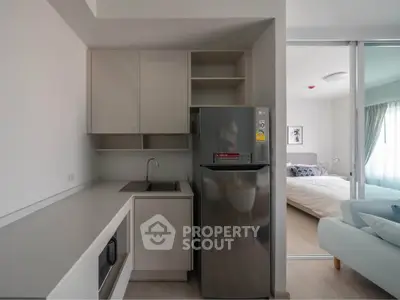 Modern compact kitchen with sleek cabinetry and stainless steel fridge adjacent to cozy bedroom.