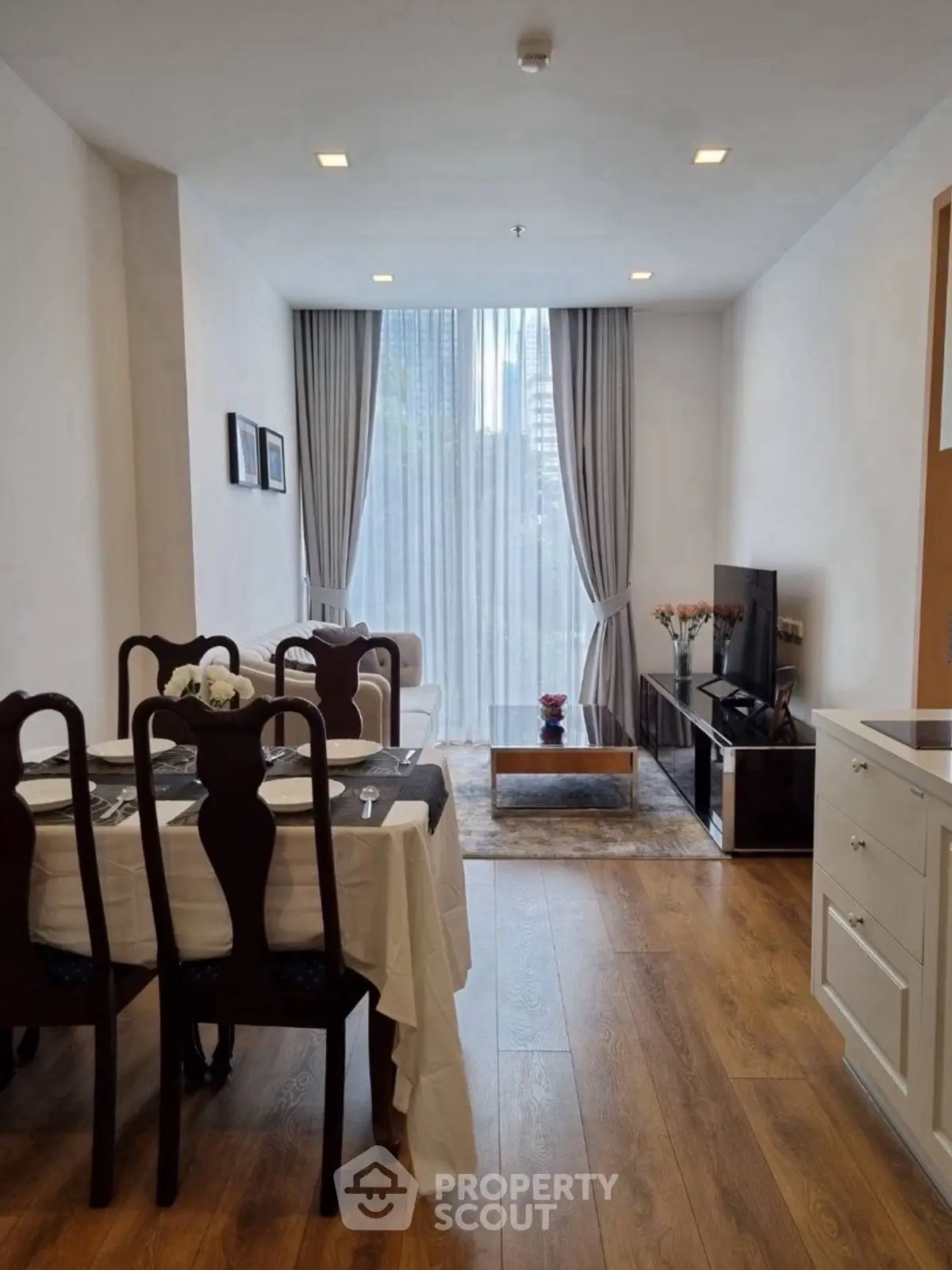 Elegant living room with dining area, wooden flooring, and large window with city view.