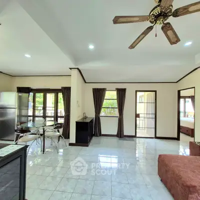 Spacious open-plan living room with dining area and ceiling fan, featuring large windows and modern decor.