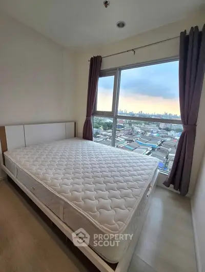 Cozy bedroom with large window offering stunning cityscape views, featuring a comfortable mattress and elegant curtains.