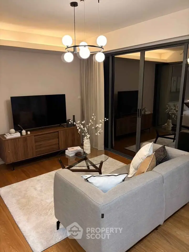 Modern living room with stylish decor and large TV, featuring a cozy gray sofa and elegant lighting.
