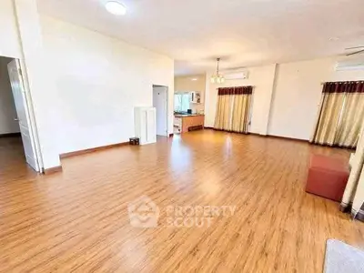 Spacious open-plan living room with wooden flooring and large windows.