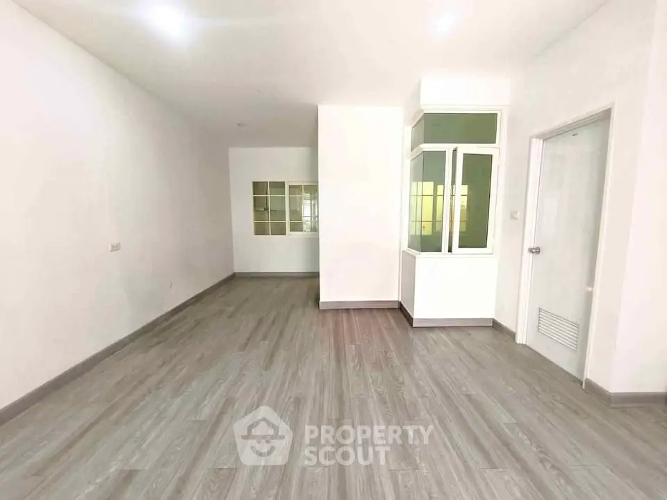 Spacious empty room with modern flooring and large window, perfect for customization.