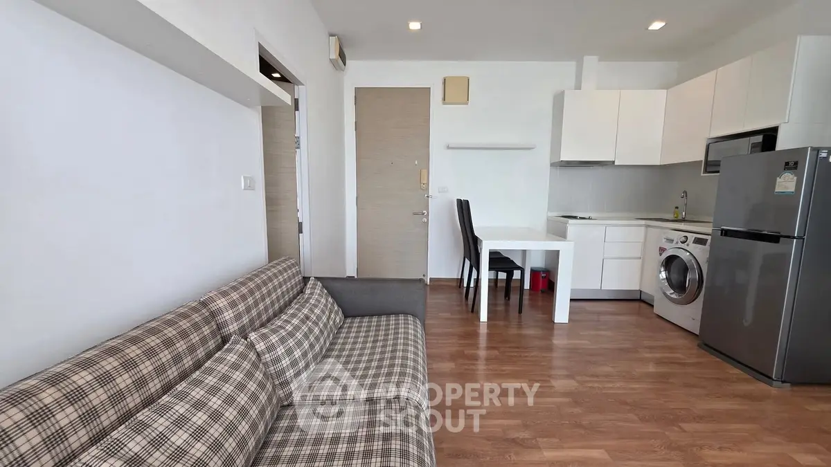 Modern open-plan living room with kitchen, featuring plaid sofa and sleek appliances.