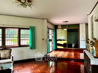 Spacious living room with wooden flooring and vintage decor, leading to a cozy bedroom.