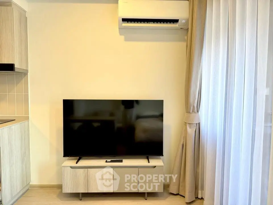 Modern living room with sleek TV setup and air conditioning, featuring elegant curtains and light wood furniture.