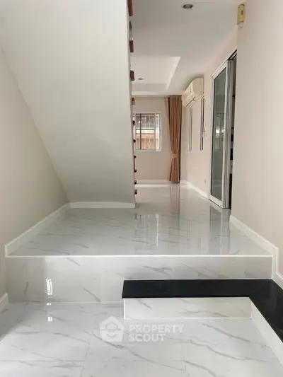 Modern interior with sleek marble flooring and staircase, featuring natural light and minimalist design.