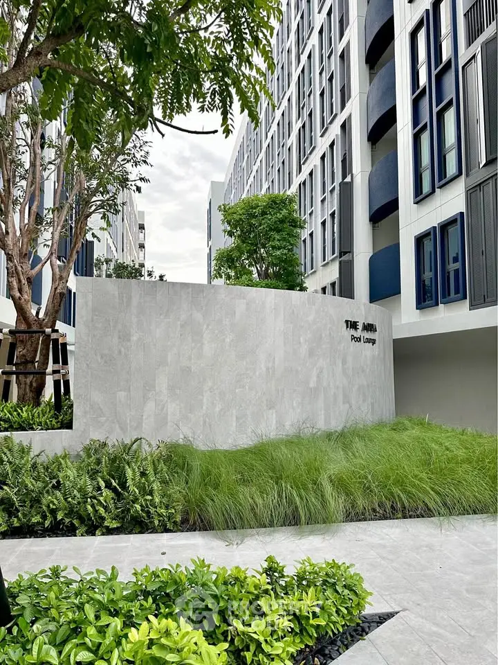 Modern residential building exterior with lush greenery and pool lounge area.
