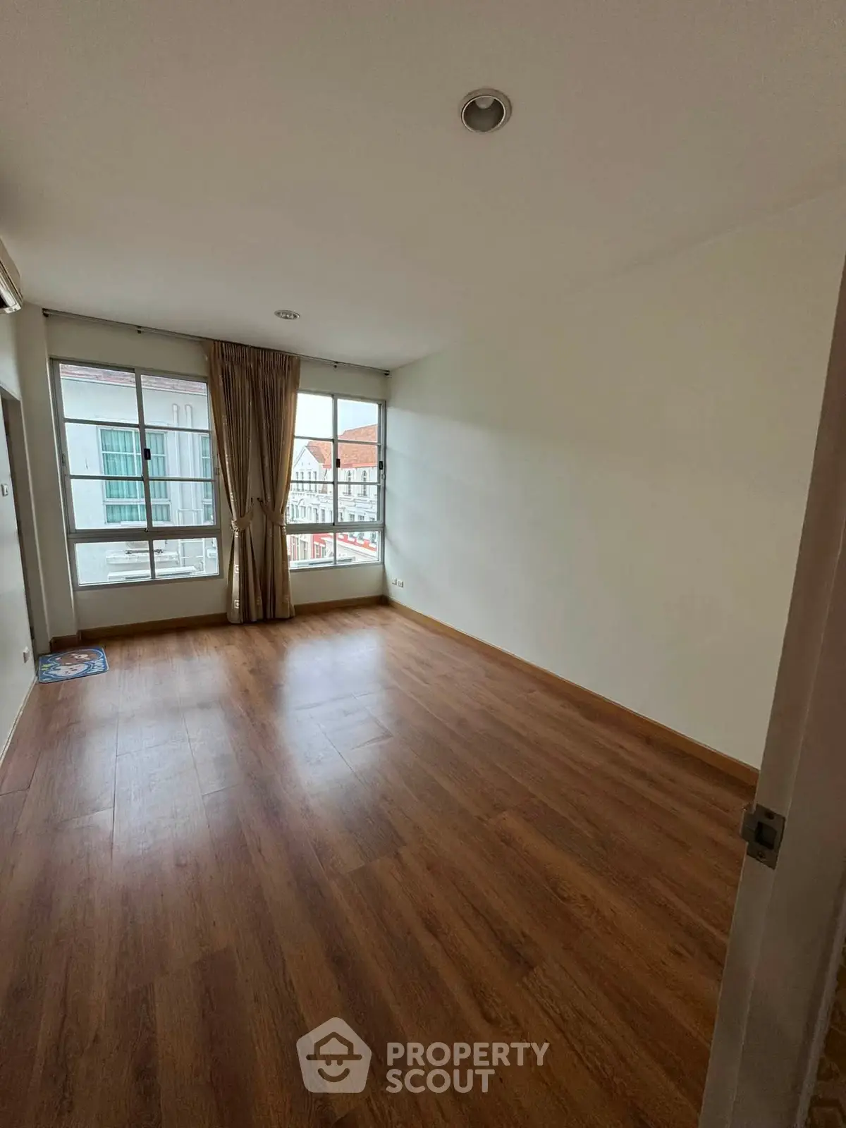 Spacious empty room with wooden flooring and large windows offering natural light.