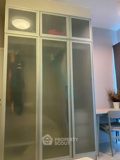 Modern bedroom with sleek frosted glass wardrobe and cozy study nook.