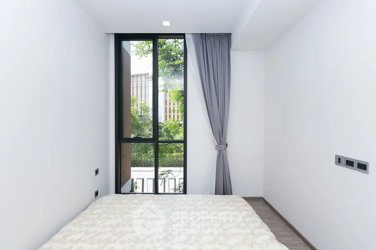 Modern bedroom with large window and elegant curtains, offering a serene view of greenery.