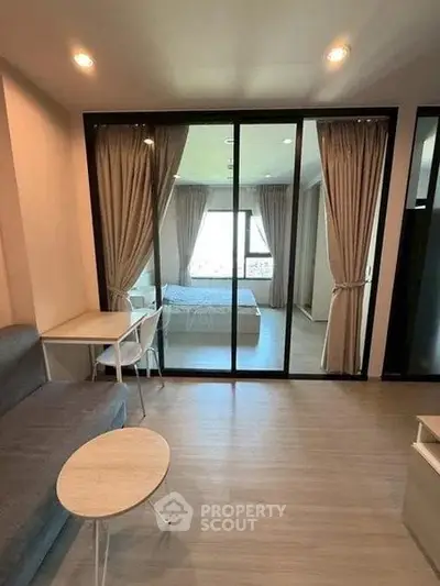 Modern apartment interior with cozy living room and view into a stylish bedroom through glass doors.