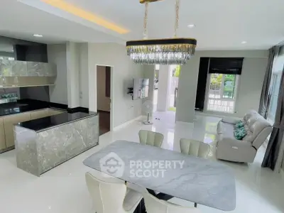 Modern open-plan living and dining area with elegant chandelier and sleek kitchen design.