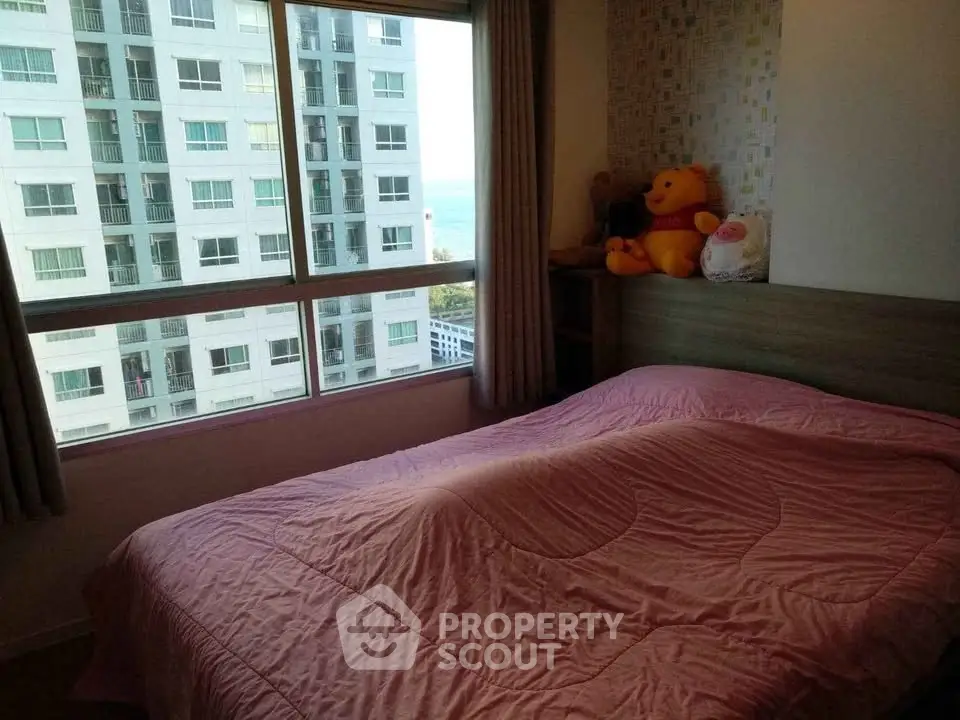 Cozy bedroom with large window offering city and sea views, featuring plush bedding and modern decor.