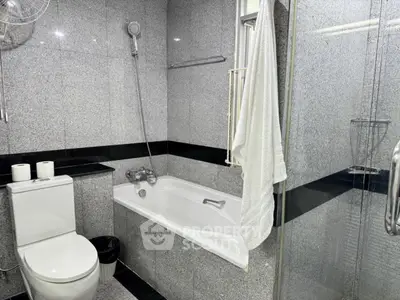 Modern bathroom with sleek gray tiles and a bathtub, featuring a glass shower enclosure.
